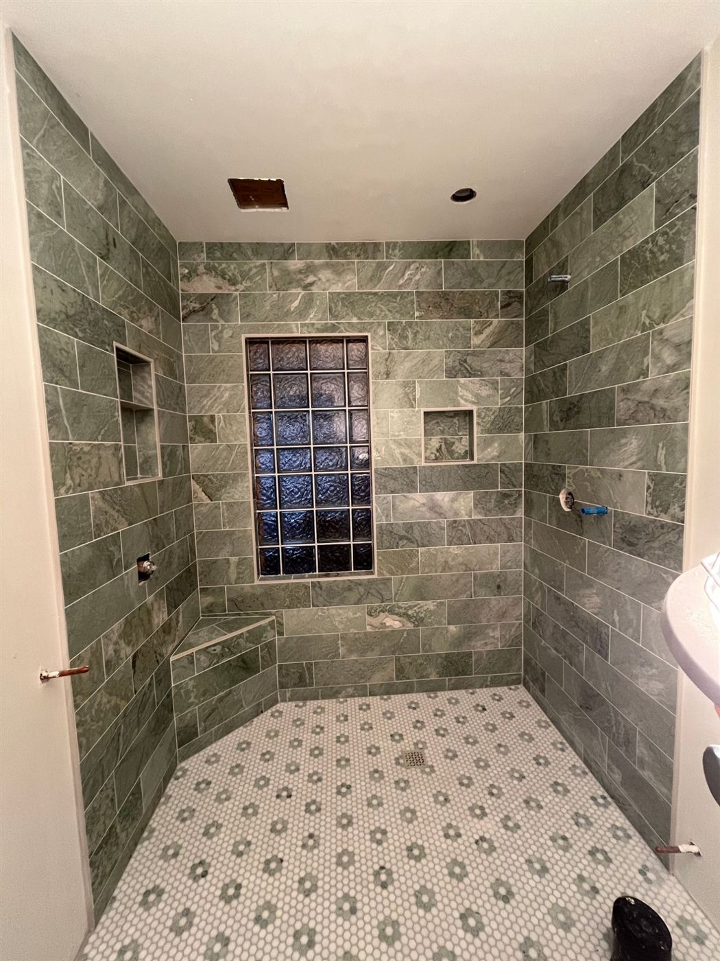 The shower finished in green stone-look tile with a white and green hex mosaic floor